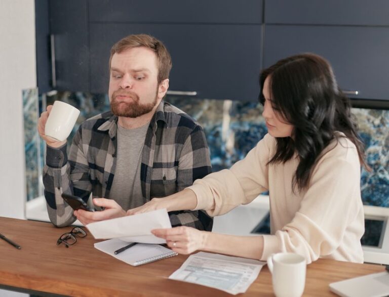 A homeowner reviews roof financing papers beside a calculator while a house with a new roof is visible outside.